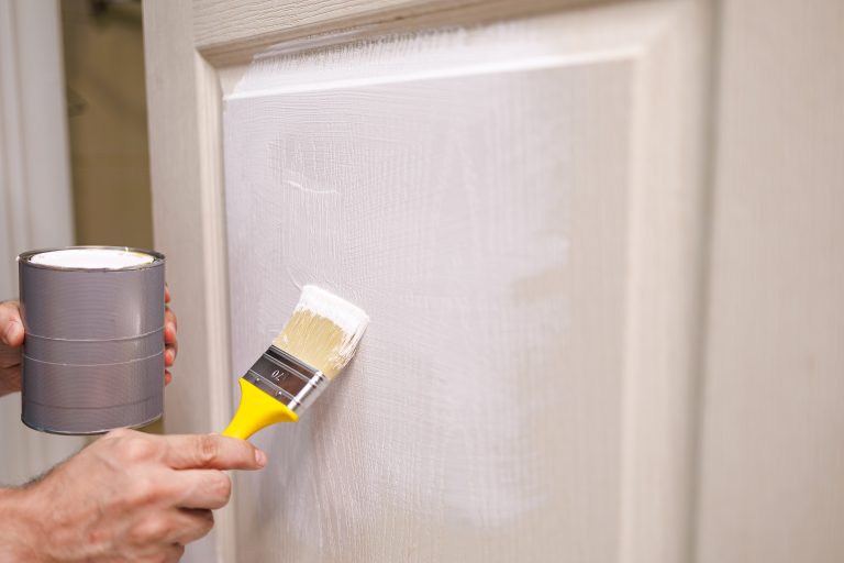 In his hands is a can of paint and a brush with which to apply the paint to the wooden door. Repair staining the doors with paint.
